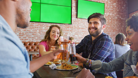 Group Of Friends Making Toast Sitting Around Table Eating Out In Sports Bar