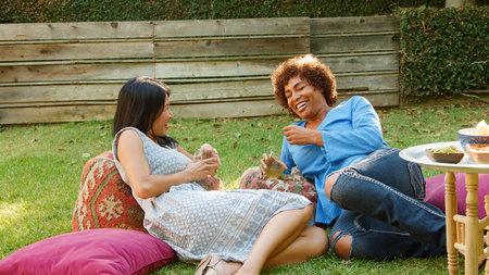 Two Smiling Mature Female Friends Enjoying Drinks And Snacks In Backyard Garden Togetherの写真素材