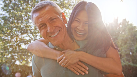 Outdoor Portrait Of Mature Couple With Woman Hugging Man From Behind With Lens Flare