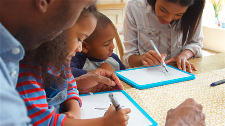 Parents And Children Drawing On Whiteboards Sitting Around Table At Table