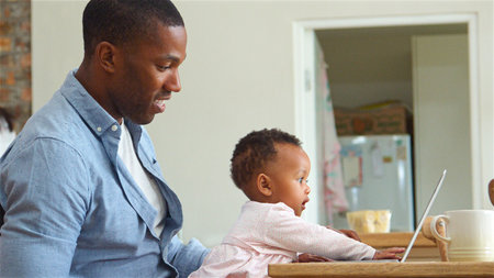 Father Holding Baby Daughter Playing With Laptop At Homeの写真素材