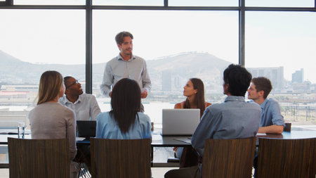 Businessman Making Presentation To Colleagues Using Laptops Sitting Around Boardroom Tableの写真素材