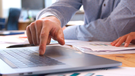 Close Up Of Businessman Sitting At Desk With Finger On Keyboard Of Laptop