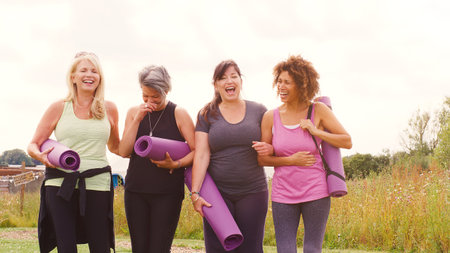 Group Of Mature Female Friends On Outdoor Yoga Retreat Walking Along Path Through Campsite
