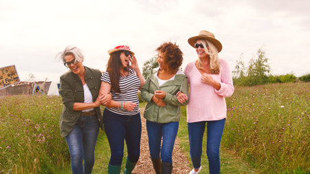 Group Of Smiling Mature Female Friends Walking Arm In Arm Along Path Through Yurt Campsiteの写真素材