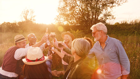 Group Of Mature Friends Making Toast As They Stand Around Fire At Outdoor Campsiteの写真素材