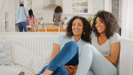 Mother With Teenage Daughter Sits On Sofa Watching TV Togetherの写真素材