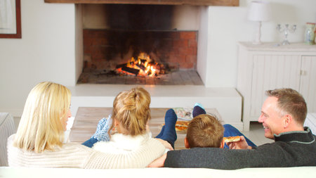 Family Sitting On Sofa In Lounge Next To Open Fire Eating Pizzaの写真素材