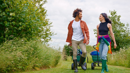 Young Couple Pulling Trolley Filled With Camping Equipment Through Field To Music Festival