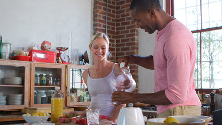 Young Couple Wearing Pajamas At Home Making Healthy Breakfast Drink With Fresh Fruit
