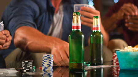 Close Up Of Group Of Male Friends Playing Cards And Drinking Beer In Loft Apartment