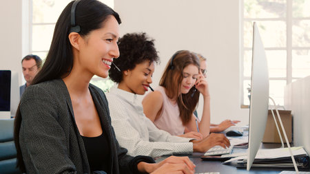 Multi-Cultural Female Business Team Wearing Headsets Working In Busy Customer Service Departmentの写真素材