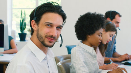 Businessman Working In Multi-Cultural Team Wearing Headsets In Customer Service Department