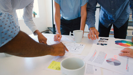 Close Up Of Multi-Cultural Business Team Standing Around Table Discussing Documents In Officeの写真素材