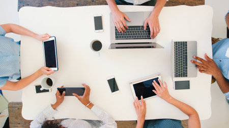 Overhead Shot Of Business Team Meeting Around Table Working On Digital Devicesの写真素材