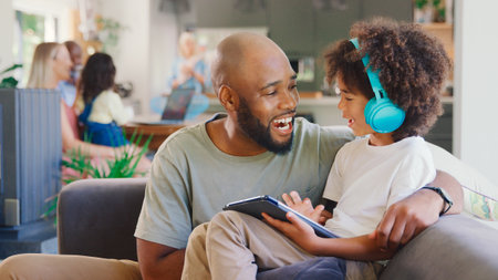 Father And Son Using Digital Tablet At Home With Multi-Generation Family In Backgroundの写真素材
