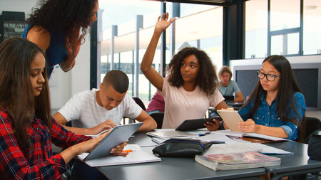 Female High School Teacher Helping Students Sitting At Desk Using Digital Tablets