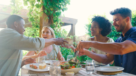 Group Of Smiling Multi-Cultural Friends Outdoors At Home Eating Meal And Drinking Wine Together
