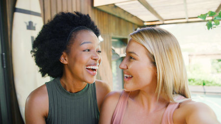 Two Smiling Female Friends Sitting At Outdoor Table At Home Talking Togetherの写真素材