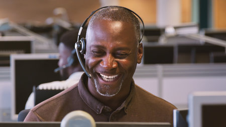 Mature Businessman Wearing Telephone Headset Working In Customer Services Department