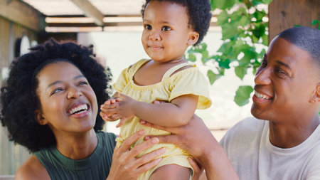 Family With Young Daughter Sitting On Table Outdoors At Home Making Video Call On Digital Tabletの写真素材