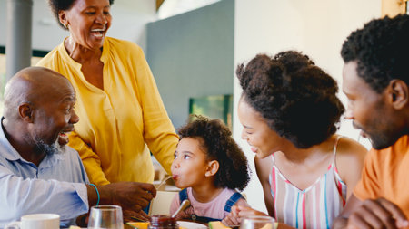 Family Shot With Grandparents Parents And Granddaughter At Breakfast Around Table At Homeの写真素材