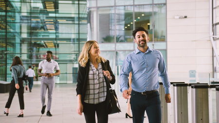Businessman And Businesswoman Talking As They Walk Through Lobby Of Modern Office Togetherの写真素材