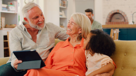 Granddaughter And Grandparents On Sofa At Home Streaming Show On Digital Tabletの写真素材