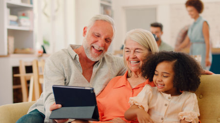 Granddaughter And Grandparents On Sofa At Home Streaming Show On Digital Tabletの写真素材