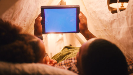 Father And Daughter At Home Lying In Indoor Tent Or Camp Watching Blue Screen Digital Tabletの写真素材