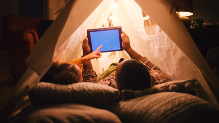 Father And Daughter At Home Lying In Indoor Tent Or Camp Watching Blue Screen Digital Tabletの写真素材