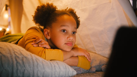 Girl At Home Lying In Indoor Tent Or Camp Watching Or Streaming To Digital Tabletの写真素材