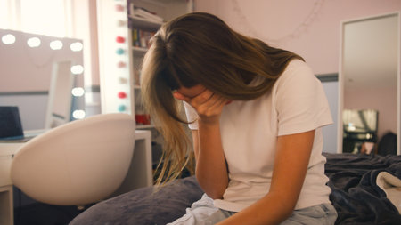 Depressed Teenage Girl Sitting On Bed At Home With Head In Handsの写真素材