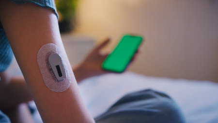 Close Up Of Diabetic Girl Sitting On Bed At Home Checking Insulin Levels On Mobile Phone Appの写真素材