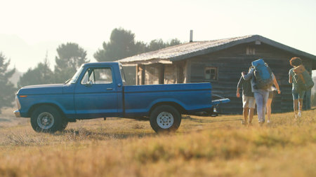 Group Of Friends Unloading Backpack From Pick Up Truck On Road Trip To Cabin In Countryside