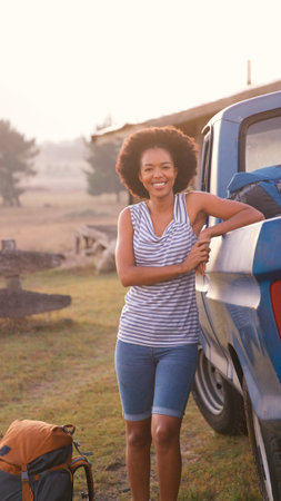 Portrait Of Young Woman Loading Backpack Into Pick Up Truck For Road Trip To Cabin In Countryside