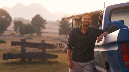 Portrait Of Smiling Young Man Loading Backpack Into Pick Up For Road Trip To Cabin In Countryside