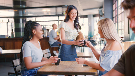 Waitress Serving Drink To Two Women Meeting In Busy Coffee Shopの写真素材