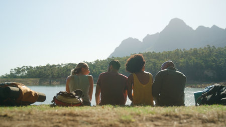 Rear View Group Of Friends On Vacation Hiking Sitting And Looking At Lake And Mountains