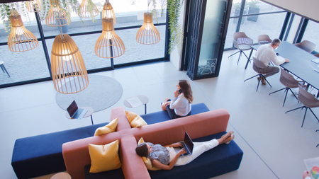 Overhead View Of Modern Open Plan Office With Staff Working Around Table And Breakout Seating Area