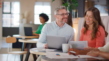 Mature Businesswoman And Businessman Working On Laptop In Informal Seating Area Of Modern Office