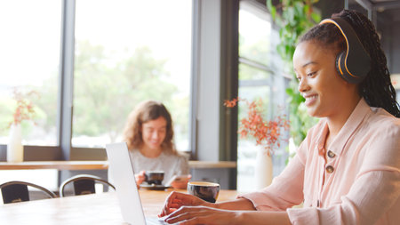 Young Businesswoman Wearing Wireless Headphones Working On Laptop In Coffee Shop
