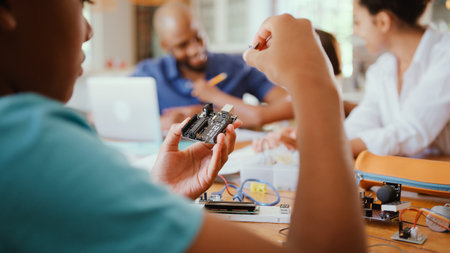 Family Around Table At Home Using Laptop With Parents Helping Children With Science Homework