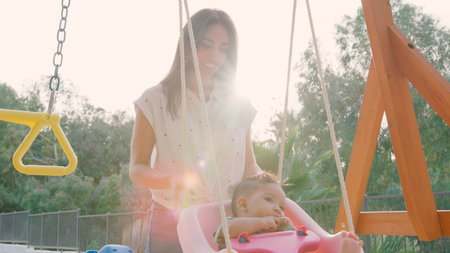 Smiling Mother Pushing Baby Son On Swings In Parkの写真素材