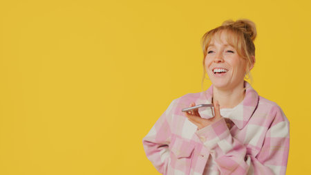 Woman Taking Phone Call On Mobile Using Mic Against Yellow Studio Background