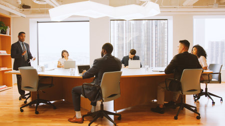 Mature Businessman Standing Giving Presentation To Colleagues Sitting Around Table In Modern Officeの写真素材