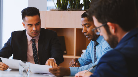 Three Businessmen Sitting Around Table Meeting In Modern Open Plan Officeの写真素材