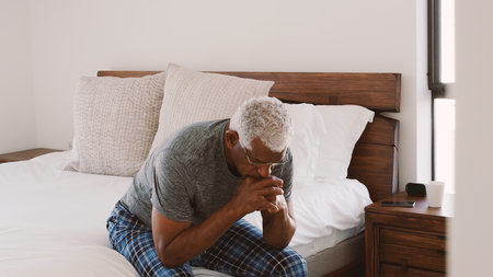Depressed Senior Man Looking Unhappy Sitting On Side Of Bed At Home With Head In Hands