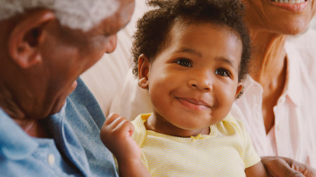 Close Up Of Grandparents Sitting On Sofa At Home Playing With Baby Granddaughterの写真素材