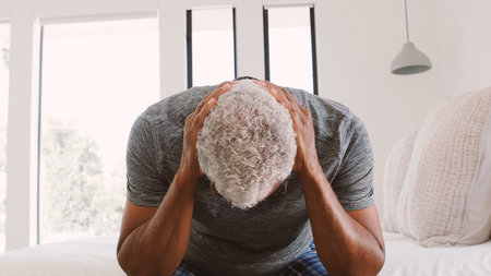 Depressed Senior Man Looking Unhappy Sitting On Side Of Bed At Home With Head In Handsの写真素材